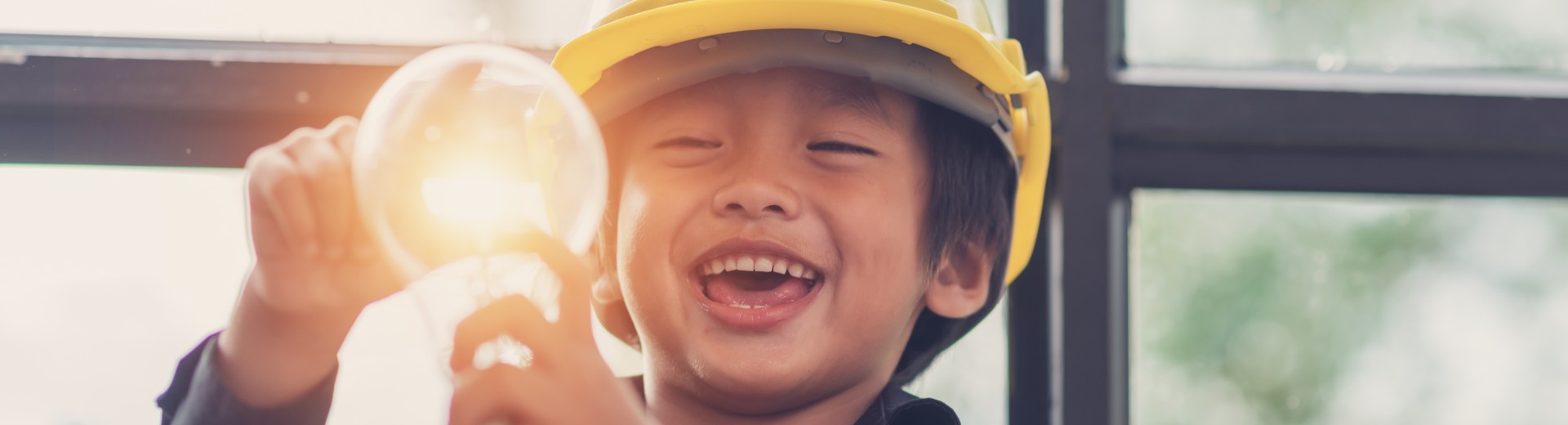 A child wearing a safety helmet holds a light bulb.