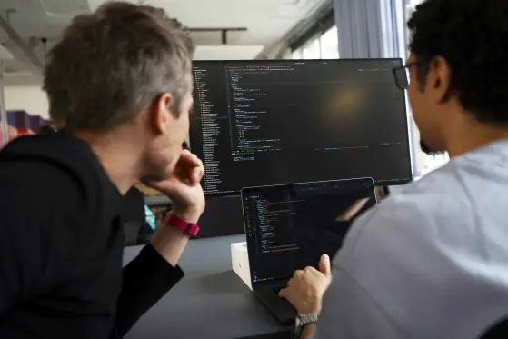 Two men reviewing lines of code on the screen.